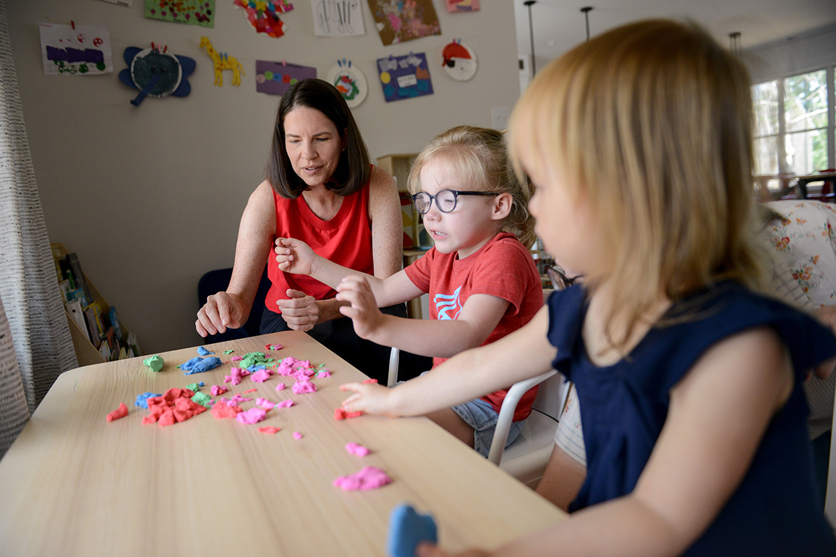 Photograph: An adult and two children playing with play dough at a child sized table with modified seating.