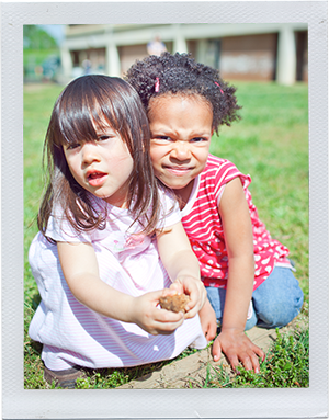 Photograph: Two preschool-aged female students play together on a grassy field. (Photograph by Alex Lazara)