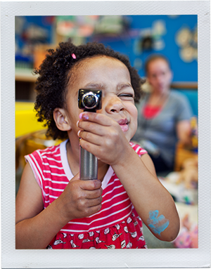Photograph: A preschool aged girl peers through an otoscope. (Photograph by Alex Lazara)