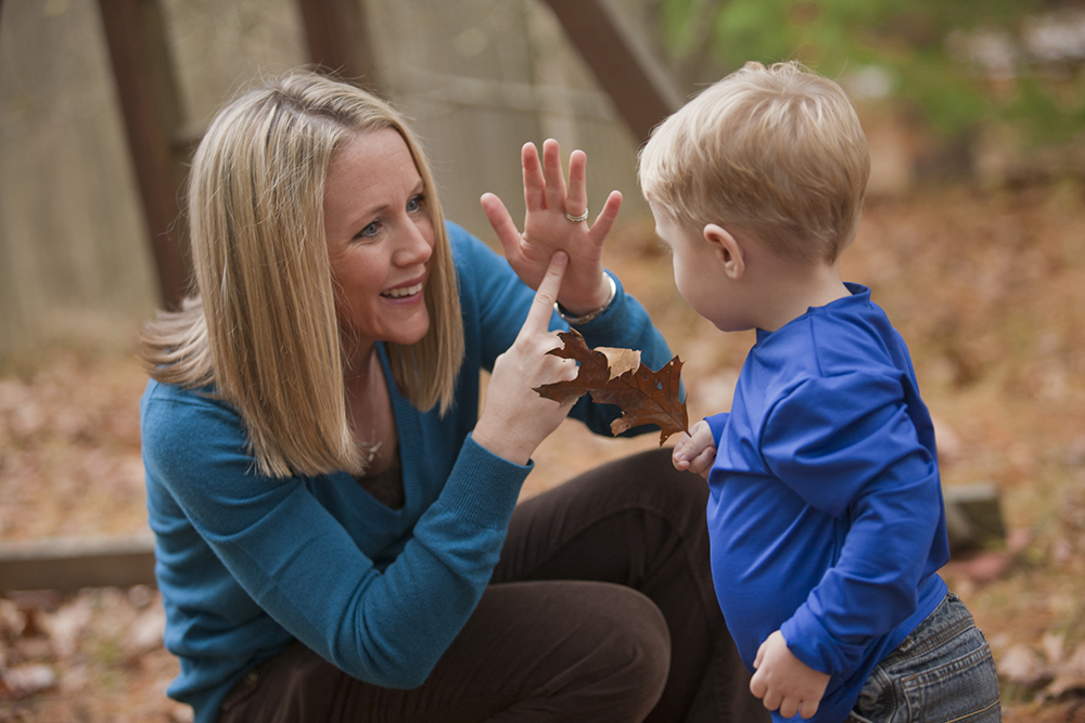 Photograph: a woman signs to a young child holding an autumn leaf.