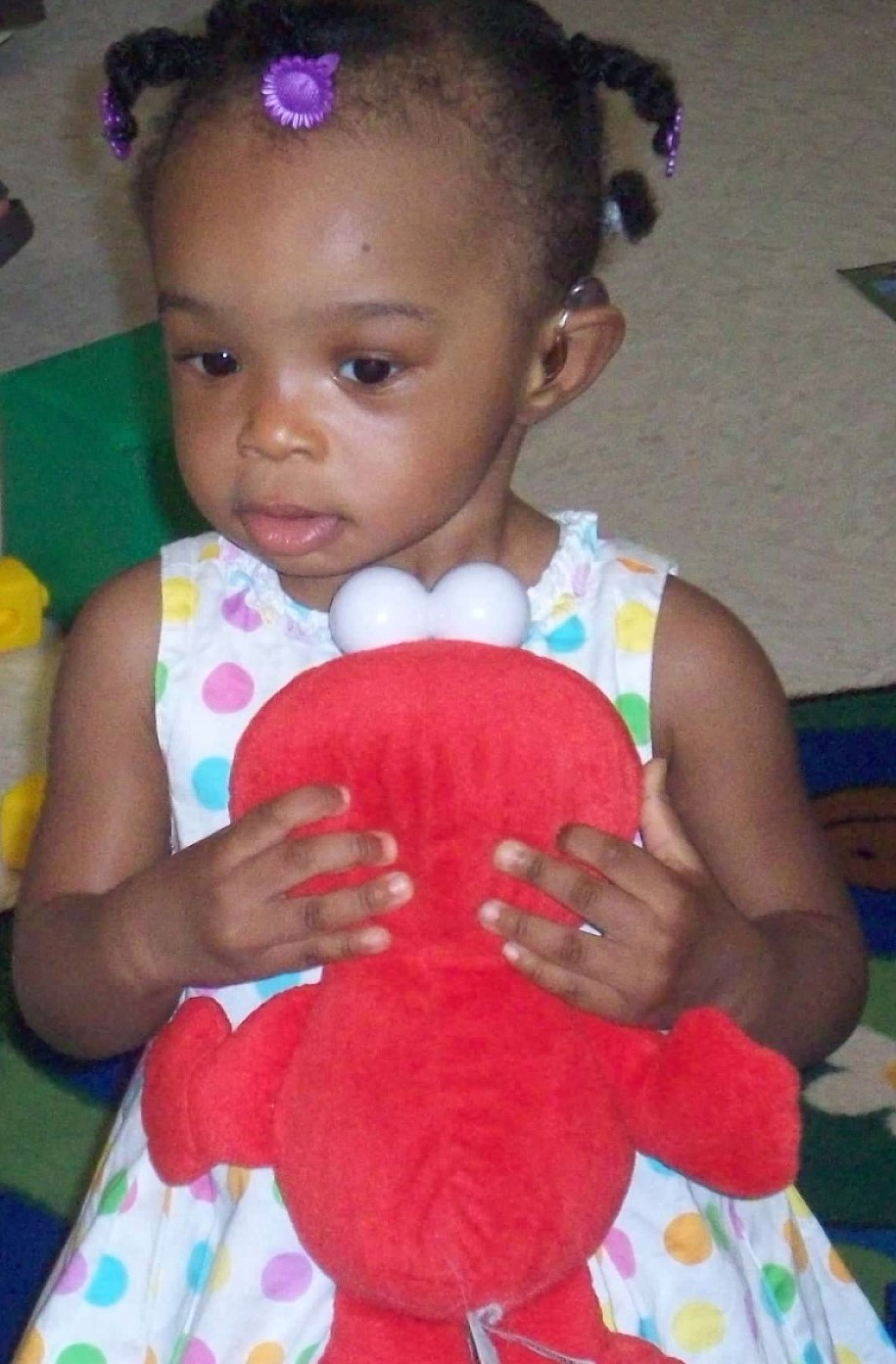 Photograph: A toddler with a hearing aid holds a red stuffed animal.