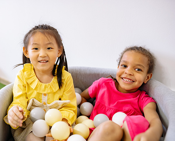 Photograph: Two young girls sit in a soft cloth tub, surrounded by plastic ball toys. (Pexels, Yan Krukov)