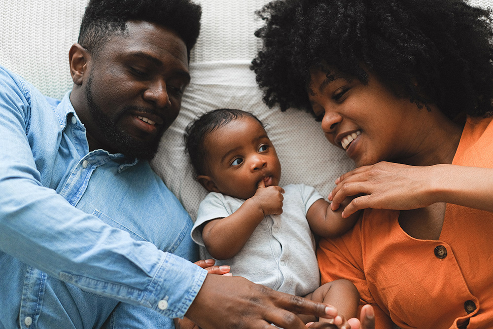 Photograph: A couple and a baby are lying together on a bed (Pexels, Anna Shvets).