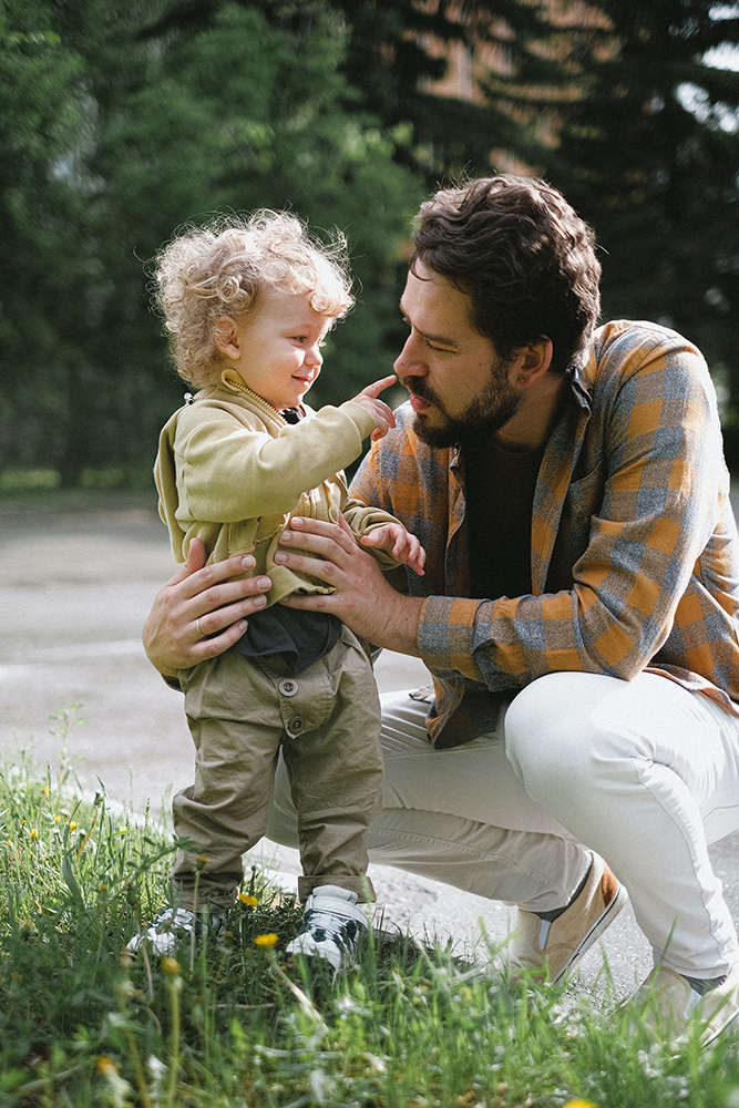 Photograph: A man holds a toddler upright. The toddler is touching his nose. (Pexels, Anna Shvets).