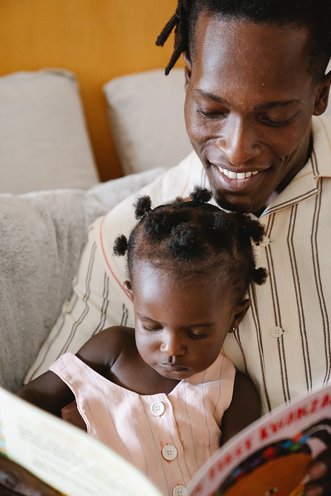 Photograph: A father holds a baby in his lap. The baby is turning pages in a book (Pexels, Greta Hoffman).