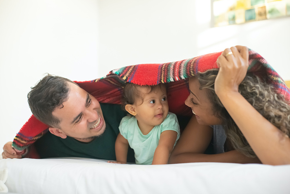 Photograph: A mother and father lie on a bed under a blanket with their infant child.