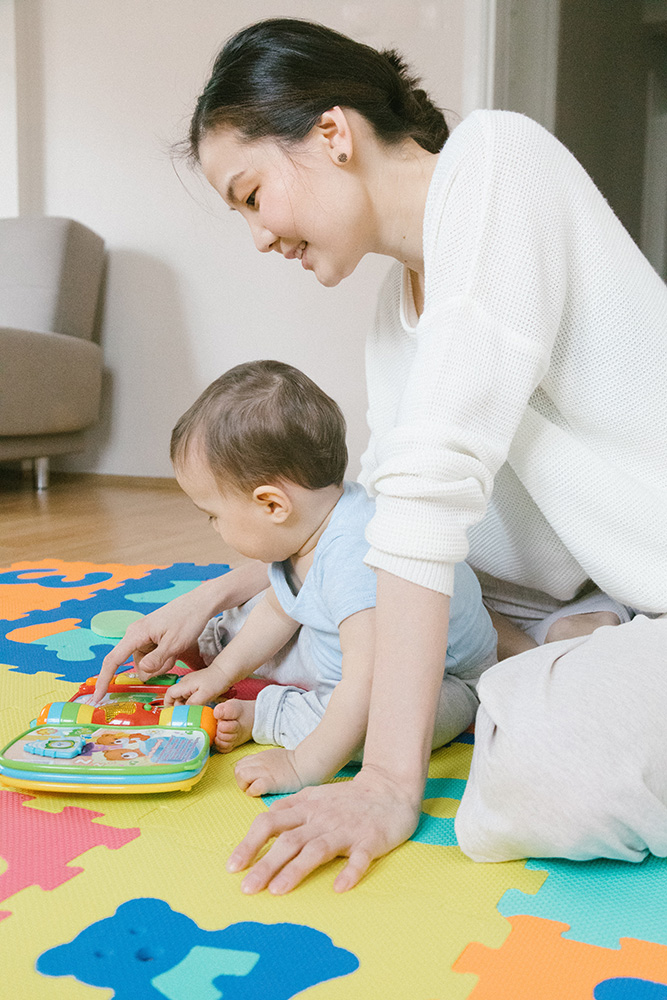 Photograph: A mother supervises as her infant child plays with a colorful plastic toy (Pexels, Meruyert Gonullu).