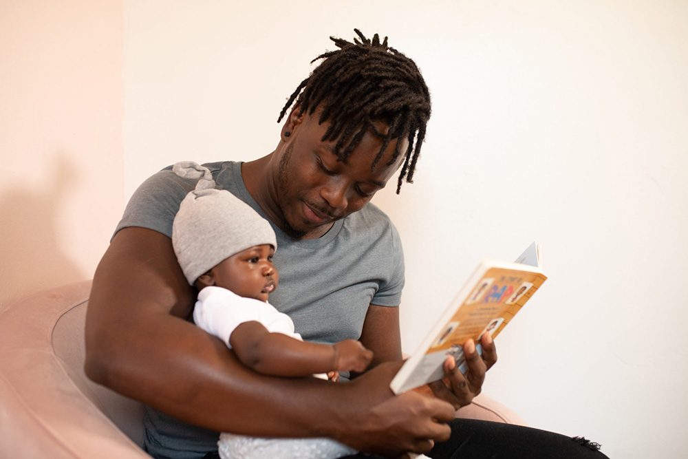 Photograph: A man holds a baby on his lap. They are looking through a picture book (Pexels, nappy).