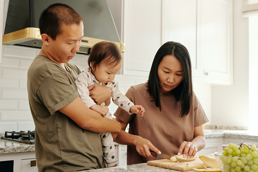 Photograph: A couple slices a banana in the kitchen while their baby watches (Pexels, Vanessa Loring).