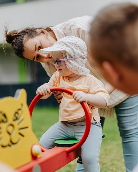 Photograph: A preschool teacher holds a child steady on one end of a see-saw.